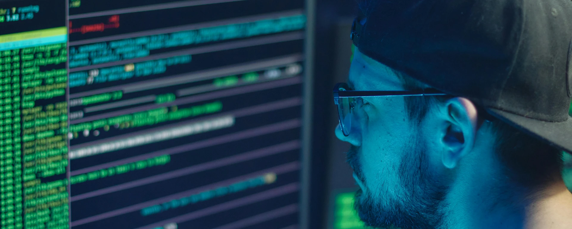 A cybersecurity expert inspecting lines of code on multiple monitors in a dimly lit office