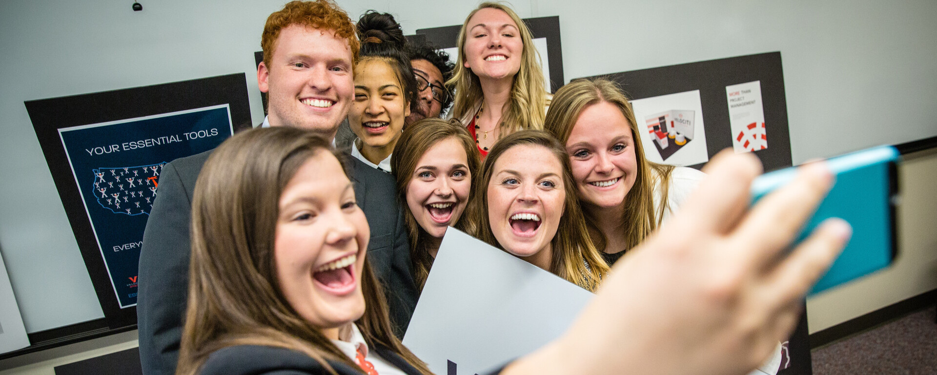A group of smiling young professionals taking a selfie together in a classroom setting with Velociti branding visible, at Northwest Missouri State University