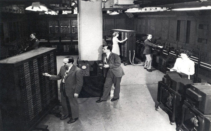 Jean & ENIAC Co-inventors | Group image of several members of the ENIAC team, 1946. Left: ENIAC co-inventors Presper Eckert and Homer Spence.  Center: ENIAC co-inventor John Mauchly. Back Center: Jean Jennings Bartik. Right: Herman Goldstine and Ruth Lichterman (U.S. Army photo from the archives of the ARL Technical Library)