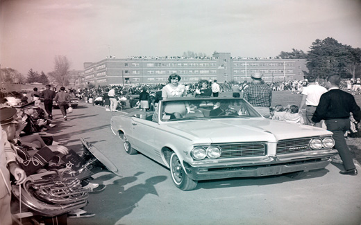 Following the 1962 Football Game, the Homecoming Queen is driven away in a convertible.