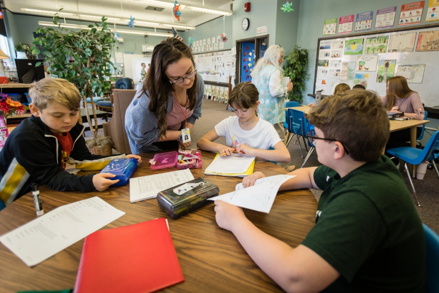 A female elementary education teacher helps three students go over their homework assignment.