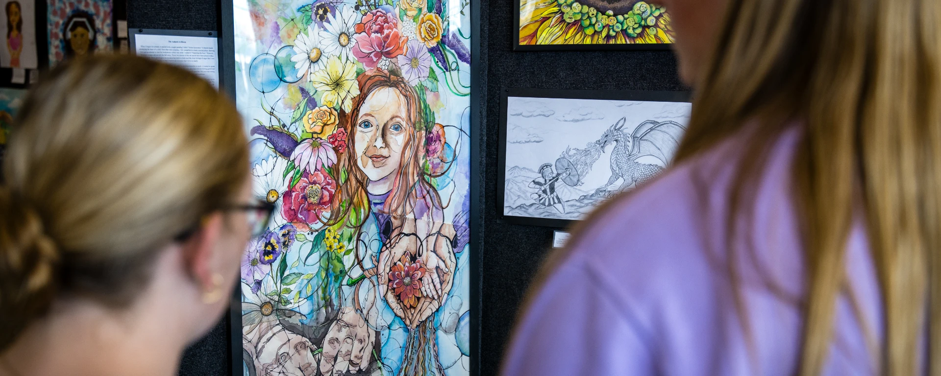Two females look at an artist drawing during I Will Listen, an annual Northwest event to help reduce stigmas surrounding mental illness through educational activities. The drawing is of a young red-headed girl, her hands posed in the shape of a heart, surrounded by colorful flowers.