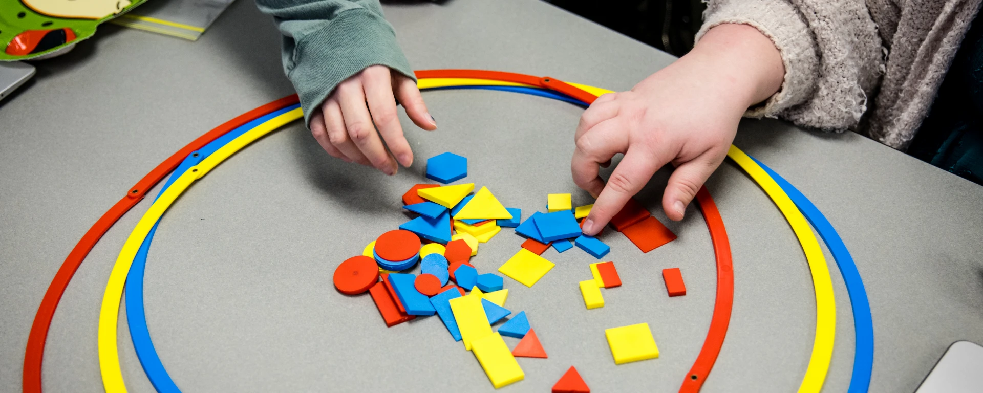 Close-up of hands sorting plastic shape pieces during a hands-on math lesson in elementary school.