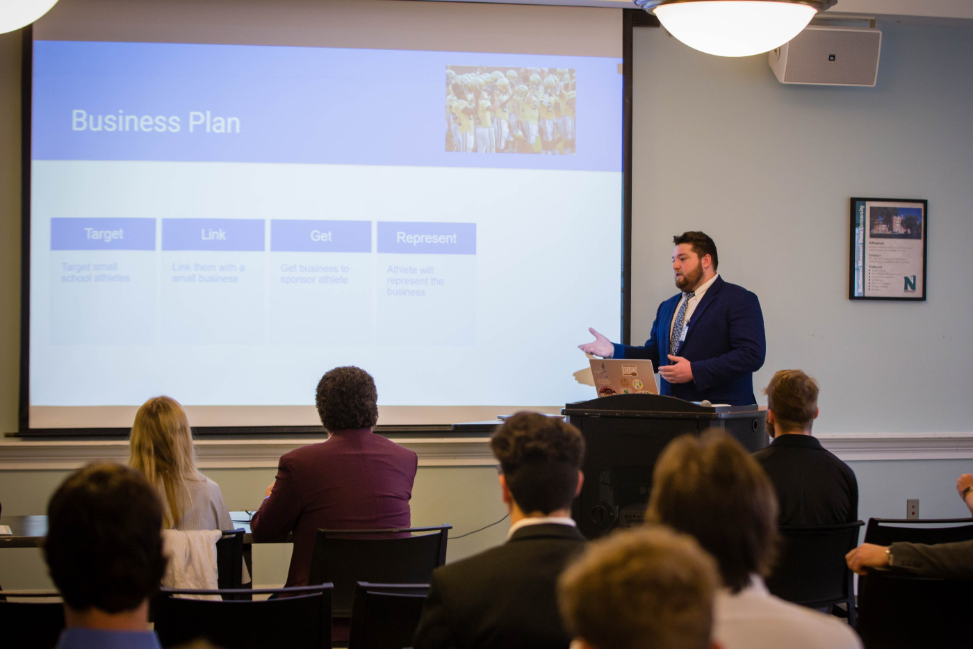 A student pitched their business ideas to a panel of business professionals during Northwest's annual New Venture Pitch competition. On the projection screen behind them is a slide detailing their business plan.