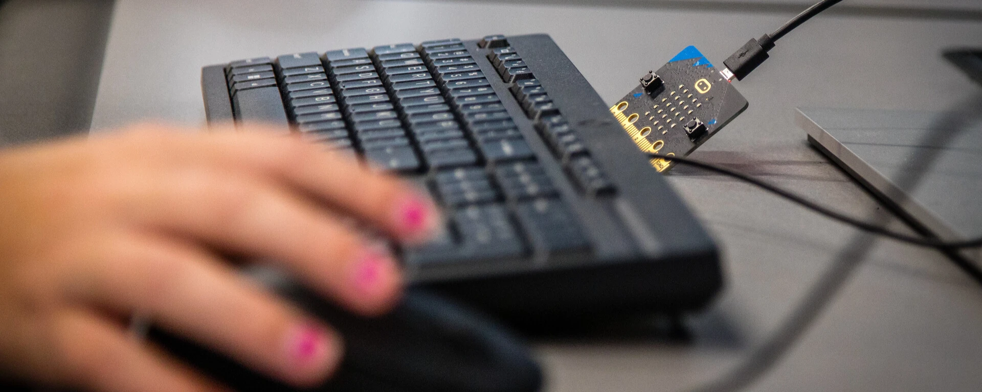 A person with pink nail polish using a black keyboard and mouse connected to a small electronic device on a desk at Northwest Missouri State University