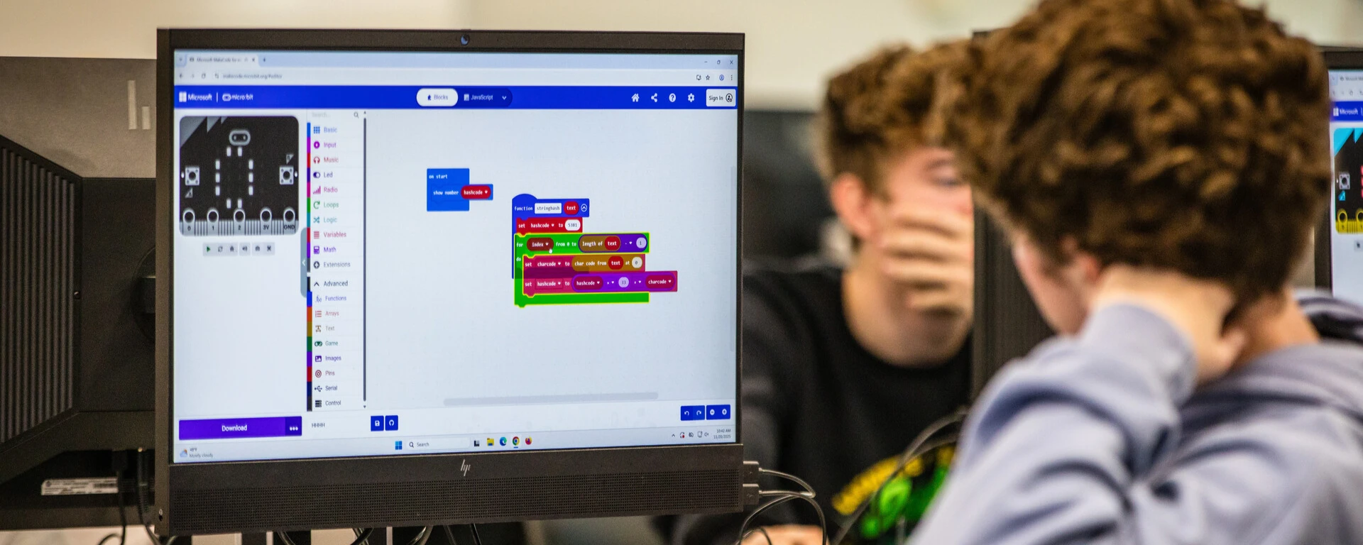 Two students viewing a computer monitor displaying a colorful block-based programming interface with code blocks in blue, pink, and green colors at Northwest Missouri State University