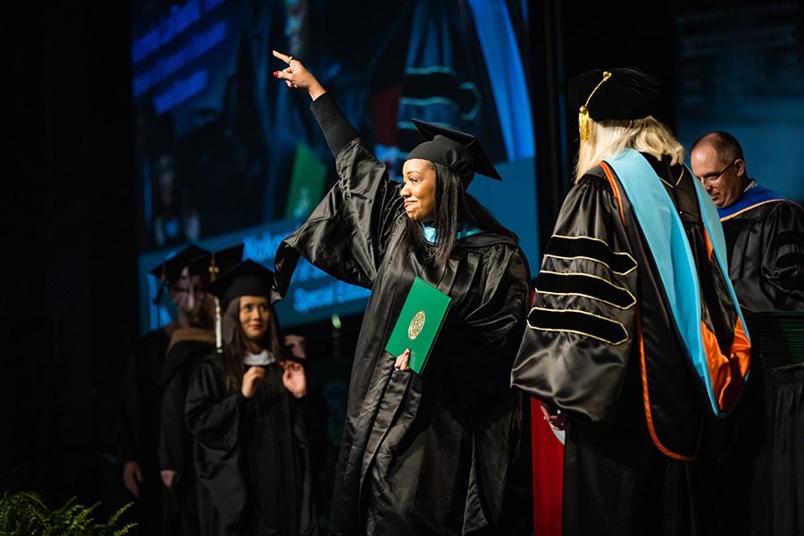 A Northwest graduate acknowledges people in the crowd as she crosses the University's commencement stage.