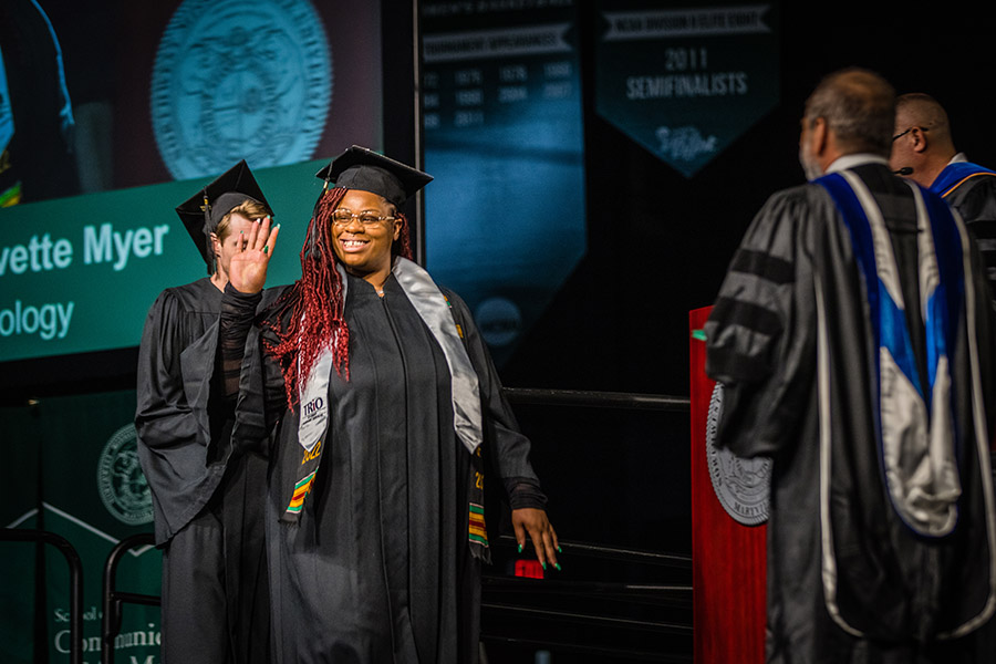 A graduating student waves to the crowd as she crosses Northwest's commencement stage.