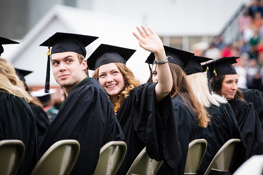 A degree candidate waves to attendees in the grandstand at Bearcat Stadium during Saturday's commencement ceremony.