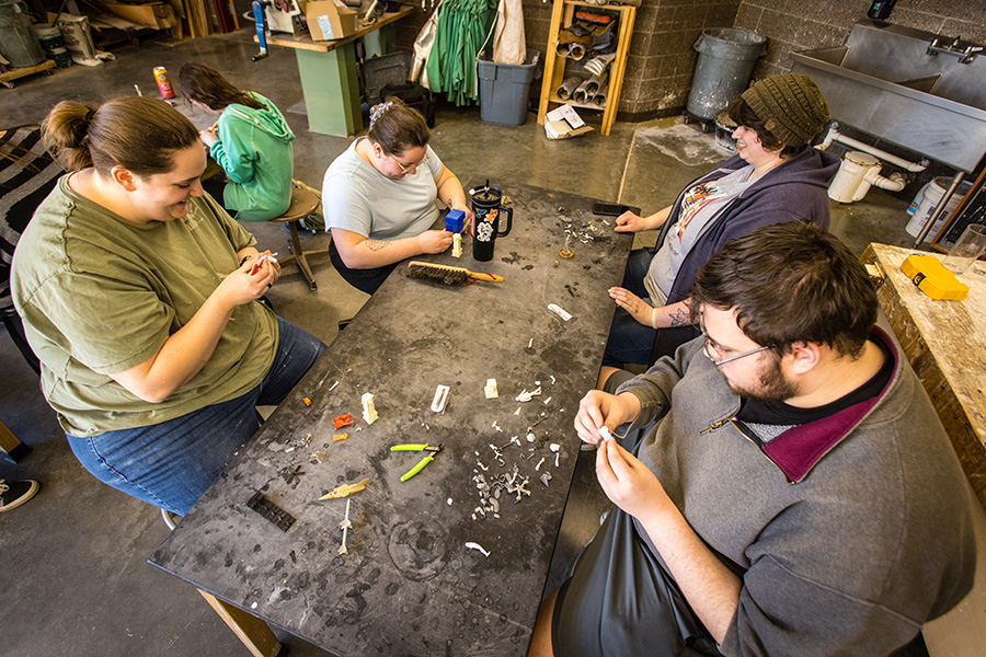 Gwendelyn Alvares and Curtis Pestel, sitting on the right side of the table, work on their sculptures during a workshop with artist Kris Kuksi.