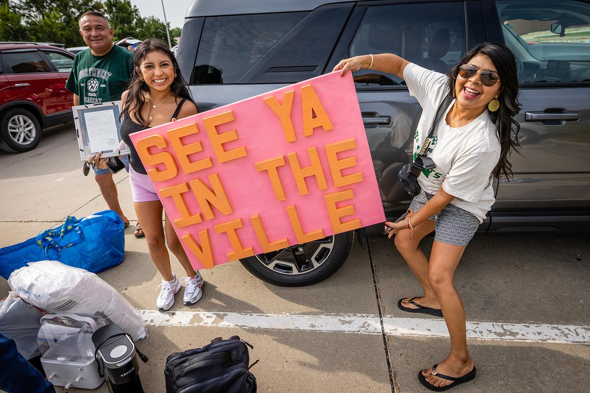 While unloading a car, a student holds up a pink sign that says 'See ya in the Ville'