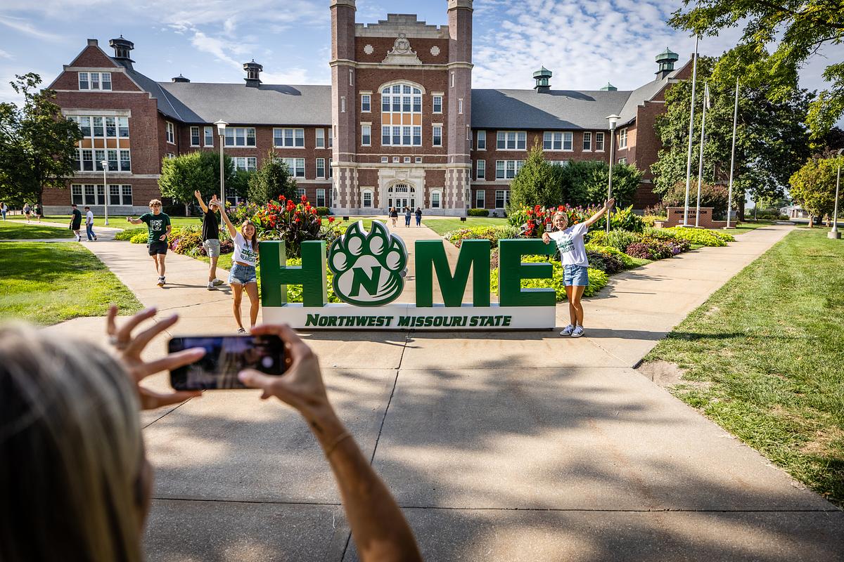 Two students pose next to large 3D 'Home' sign in front of the Administration Building