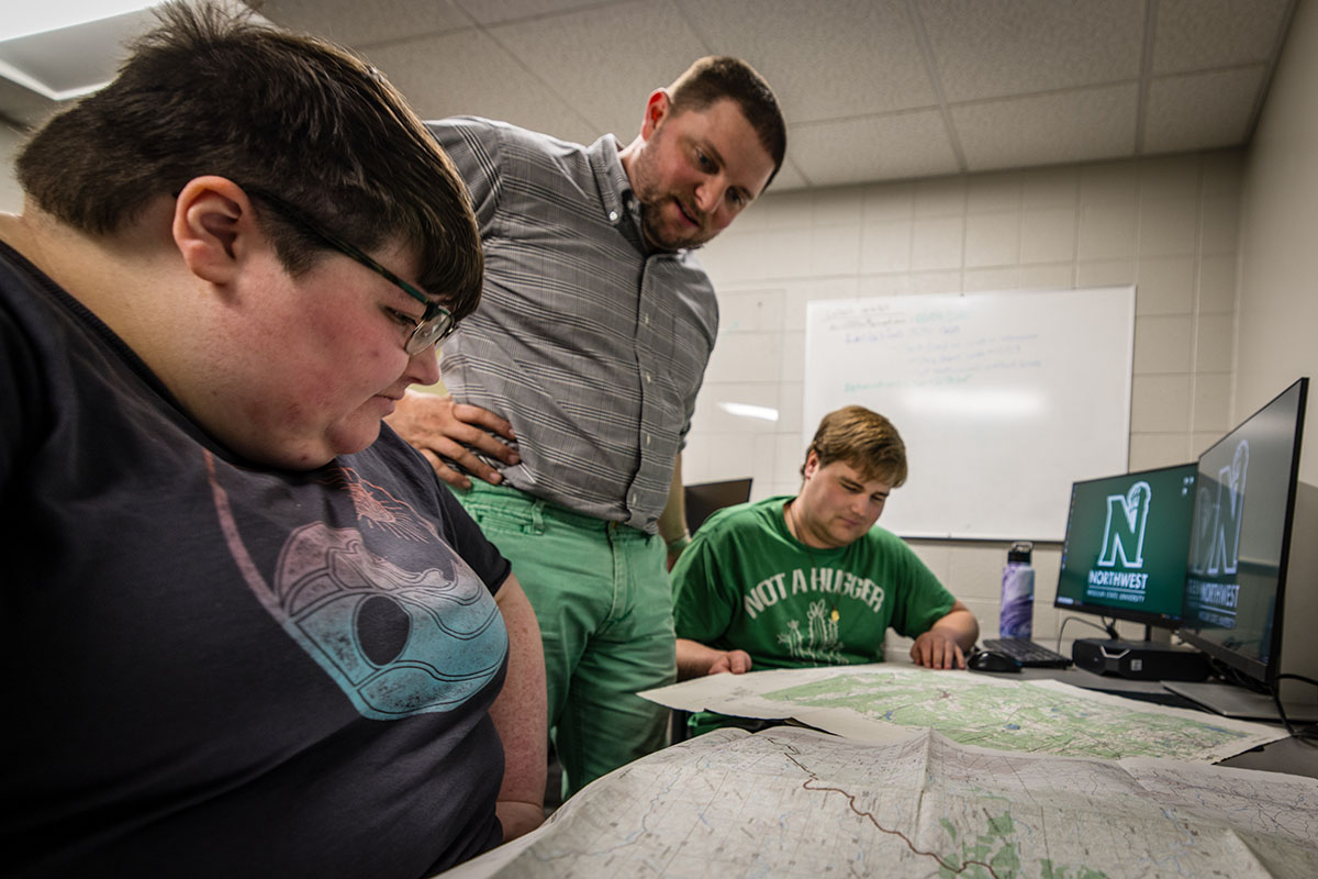 Dr. Brett Chloupek (center) looks over a pair of maps with Northwest students Nikki Welch and Joseph Sullivan, who actively edit and update topographic maps through a partnership with the National Geospatial-Intelligence Agency. (Photo by Lilly Cook/Northwest Missouri State University)