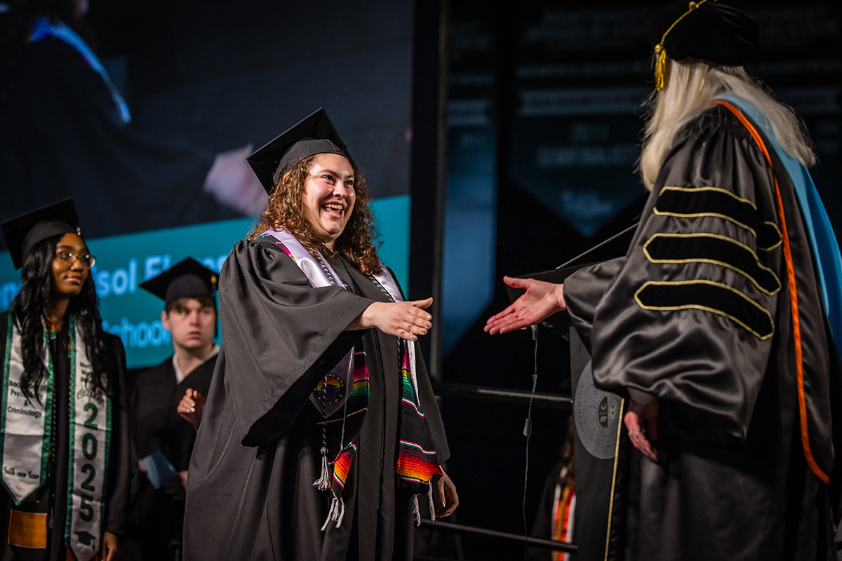 A Northwest graduate reaches toward Provost Dr. Jamie Hooyman for a handshake while crossing the commencement stage Saturday morning. (Photo by Todd Weddle/Northwest Missouri State University)