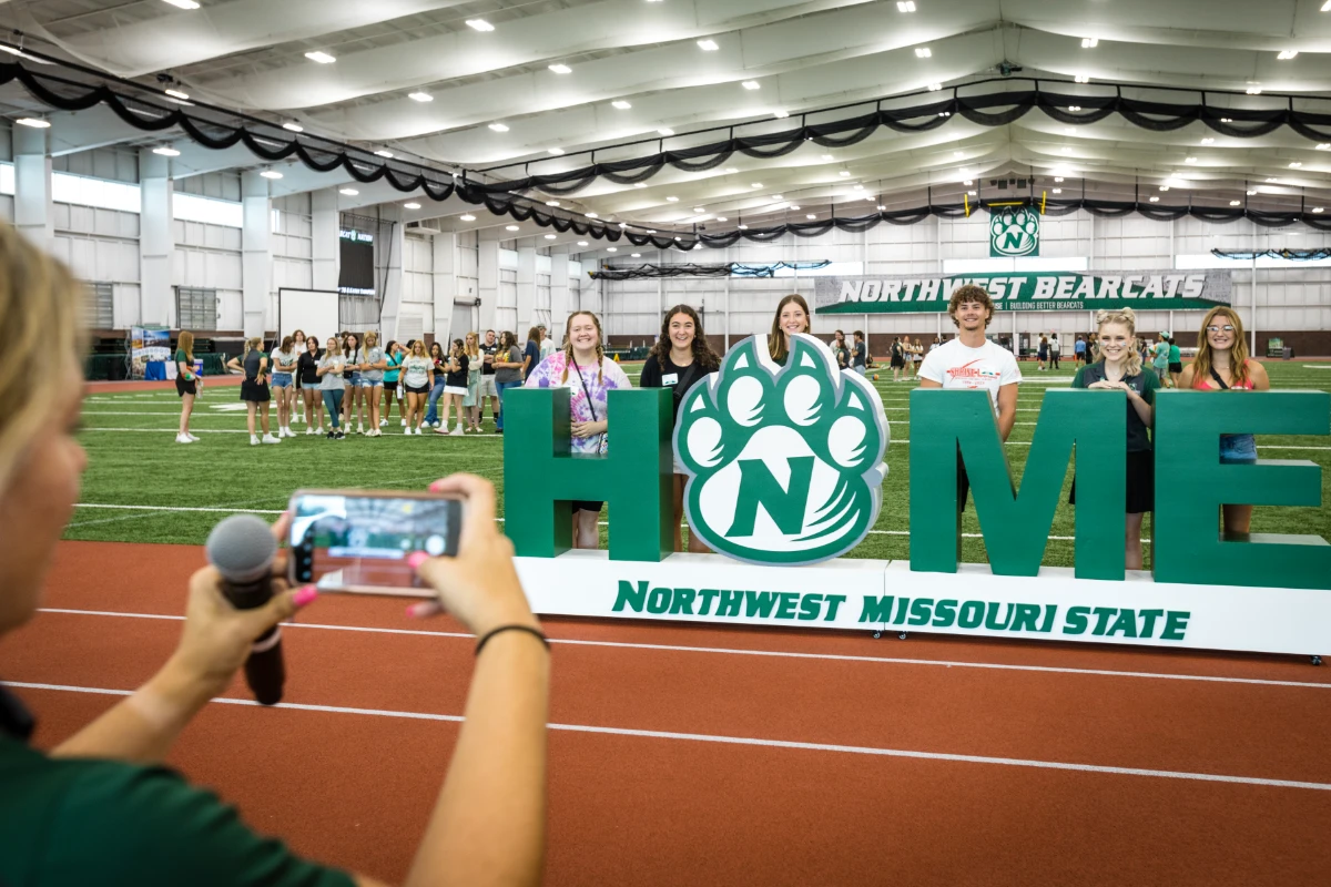 Students take a picture with the Northwest Home sign at the Hughes Fieldhouse, where the student services fair is held before the first SOAR session begins.