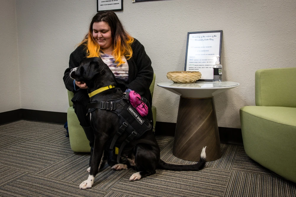 Female student seats in a chair while petting her service dog